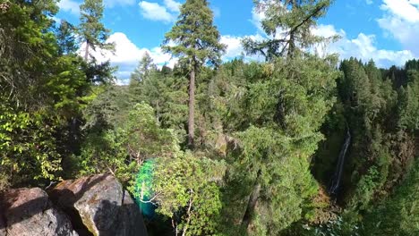 Pan-over-a-forested-canyon-with-a-waterfall-in-the-distance