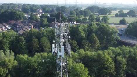 5G-broadcasting-tower-antenna-in-British-countryside-with-vehicles-travelling-on-highway-background-rising-aerial-view