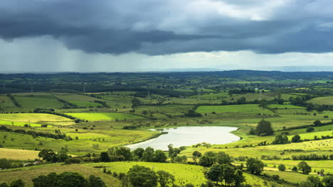 Time-lapse-of-rural-farming-landscape-with-grass-fields,-lake-and-hills-during-a-passing-storm-rainy-day-in-Ireland