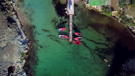 Dolly-in-overhead-view-of-a-small-wooden-walkway-with-fishing-boats-on-either-side,-Kanoa-Beach,-Curacao,-Dutch-Caribbean-island