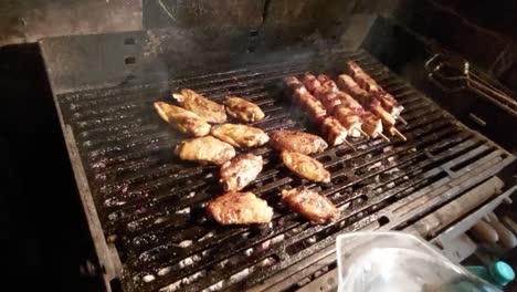 Turning-over-chicken-wings-and-skewers-on-hot-charcoal-barbecue-and-removing-finished,-done-meat