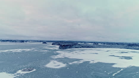 Aerial-backward-moving-shot-of-frozen-blue-lake-with-pattern-underwater-in-beautiful-winterscape-on-a-cloudy-day