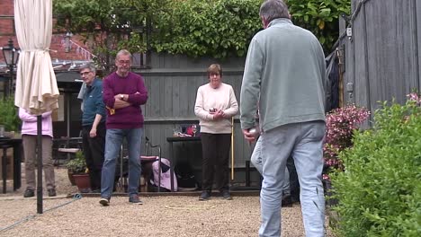 A-game-of-pétanque-being-played-on-a-gravel-track-between-two-teams-of-men-and-women