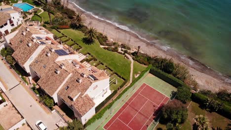 Aerial-Birds-Eye-View-Over-Beach-Side-Properties-With-Tennis-Court-In-Estepona,-Costa-del-Sol