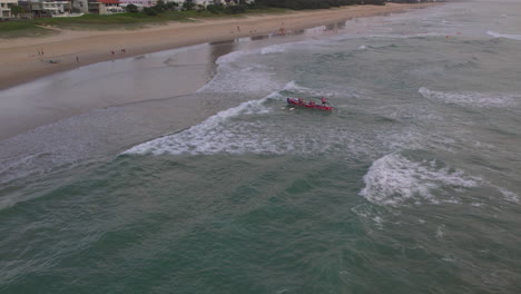 Aerial-view-of-Mermaid-Beach-SLSC-race-boat-coming-into-shore-during-a-training-session-with-the-popular-Gold-Coast-city-in-the-background-along-Mermaid-Beach-Gold-Coast-QLD-Australia