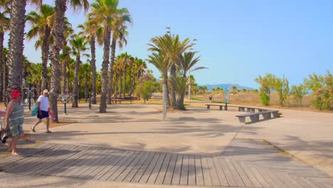 Grau-Area-With-Tourists-Walking-On-The-Wooden-Boardwalk-Leading-To-Pinar-Beach-In-Castellon,-Spain---wide-shot