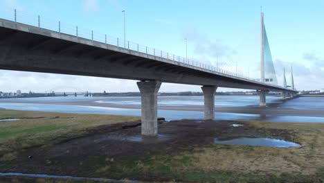 Mersey-gateway-landmark-toll-bridge-at-low-tide-with-river-marshland-aerial-view-low-orbit-right