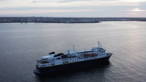 Barco-Explorador-Natgeo-Flotando-Tranquilamente-Con-Islandia-Reykjavik-En-El-Fondo,-Día-Nublado