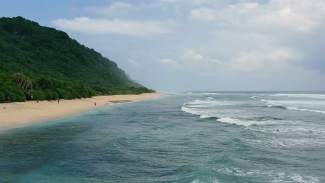 coastline-beach-with-ocean-waves-crash-on-island-with-tall-mountains,-aerial