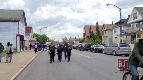 Backward-moving-shot-a-group-of-police-march-ahead-in-Buffalo-city,-United-States-at-the-sight-of-a-tragic-mass-homicide-surrounded-by-residential-houses-on-the-cloudy-day