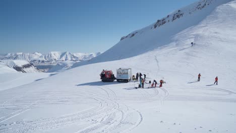 Group-of-hikers-transported-by-tracked-vehicle-near-snowy-mountain-slope-to-start-hiking