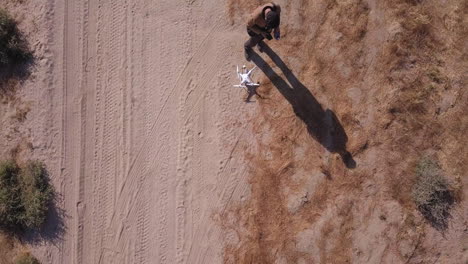 Der-Junge-Mann-Bereitet-Sich-Darauf-Vor,-Eine-Weiße-Drohne-Von-Einer-Trockenen-Sandstraße-In-Der-Wüste-Zu-Starten