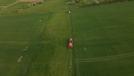 aerial-shot-of-a-tractor-with-spraying-materials-leaving-the-huge-green-meadows-after-his-work