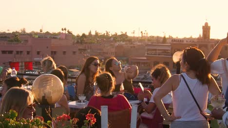 4K-Footage-of-woman-tourists-taking-pictures-with-her-smartphones-on-a-rooftop-during-sunset-at-djemaa-el-Fnaa-market,-Marrakech,-Morocco