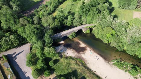 Aerial-drone-backward-moving-shot-flying-over-a-medieval-bridge-Das-Partidas-placed-over-the-river-Tea,-at-the-outskirts-of-the-town-of-Ponteareas,-Spain