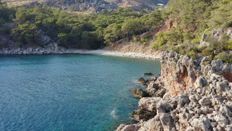 Flight-along-rocky-cliff-edge-reveal-idyllic-Turkish-azure-blue-water-bay