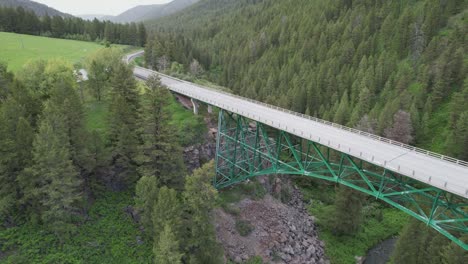 Drone-is-rising-above-a-steel-bridge-at-the-mouth-of-a-pine-covered-canyon