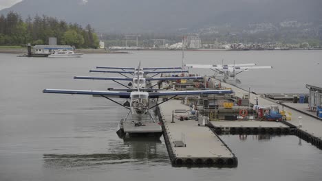 Vista-De-Los-Hidroaviones-Atracados-En-Línea-En-El-Centro-De-Vuelo-Del-Puerto-De-Vancouver,-La-Bahía-Del-Mar-Y-Las-Montañas-En-El-Fondo,-Columbia-Británica,-Canadá