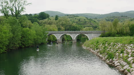 Hermosa-Toma-De-Drones-Al-Lado-Del-Río-Con-Naturaleza-Verde-Y-Un-Gran-Puente-De-Arco-Para-Autos