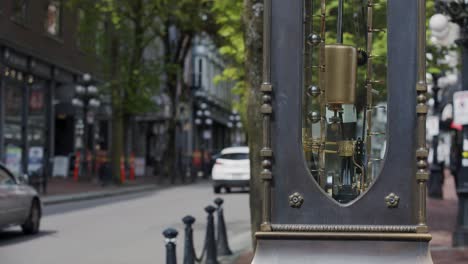 Close-up-of-famous-Gastown-steam-clock-pendulum-moving,-cars-driving-in-background,-Vancouver,-British-Columbia,-Canada