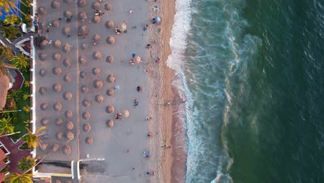 tourists-at-Los-Muertos-Beach-with-straw-umbrellas-at-sunset-in-Puerto-Vallarta-Mexico,-aerial-top-down