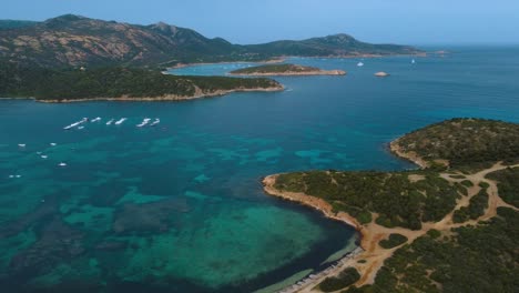 Aerial-of-an-idyllic-natural-rocky-coast-beach-sandy-bay-on-the-tourist-vacation-island-Sardinia-in-Italy-with-sun,-clear-blue-turquoise-and-calm-water-close-to-Costa-Rei