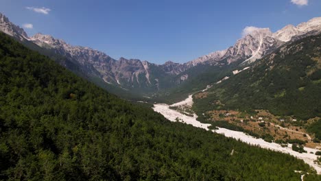 Great-valley-of-Valbona-national-park,-riverbed-surrounded-by-green-forest-trees-and-high-mountains