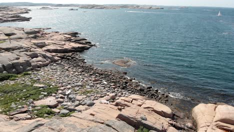 Aerial-pull-out-shot-capturing-the-unspoiled-calm-shimmering-blue-sea-and-barren-rocks-against-the-open-horizon-in-summer,-Bohuslan-coast,-Sweden