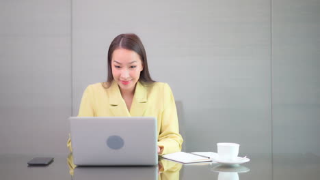 Chinese-business-lady-working-on-laptop-at-desk-celebrates-success-by-pumping-fist
