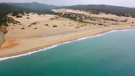 Flying-above-seaside-island-Sardinia-in-Italy-at-a-natural-dune-landscape-at-a-tourist-vacation-sea-coast-sand-beach-sandy-bay-with-clear-blue-turquoise-water