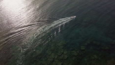 Motorboat-leaves-white-wake-trail-over-shallow-transparent-sea-waters,-Puglia-in-Italy