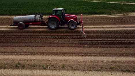 Drone-flight-near-tractor-drives-over-field-and-pours-young-lettuce-plants-with-water