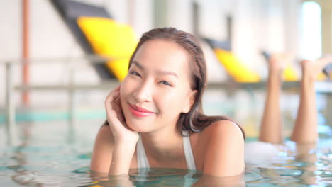 Portrait-of-Young-Happy-Beautiful-Asian-Woman-Lying-in-Spa-Center-Swimming-Pool-and-Smiling-To-Camera,-Full-Frame