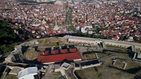 Flying-over-beautiful-city-of-Prizren,-revealing-ancient-castle-with-stone-walls-on-hill