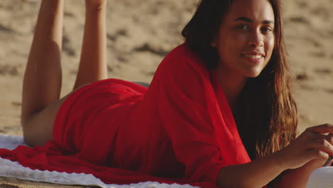 Latino-Woman-Lying-Down-on-her-Front-on-Sandy-Beach-looks-at-Camera-with-Cheeky-Smile