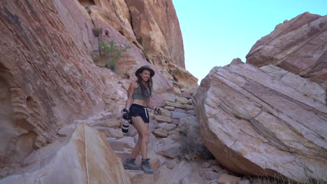 Young-Female-With-Photo-Camera-Walking-Down-the-Rocky-Hill-in-Valley-of-Fire-State-Park,-Nevada-USA,-Slow-Motion