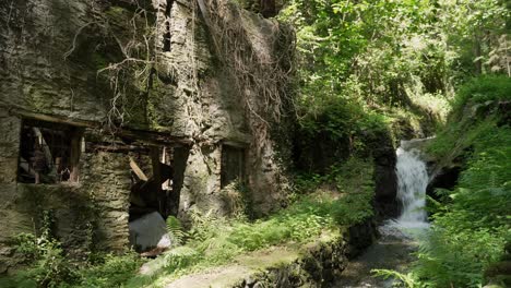 Blick-Auf-Ein-Altes-Verlassenes-Haus,-Das-Im-Wald-In-Der-Nähe-Eines-Kleinen-Wasserfalls-Auseinanderfällt