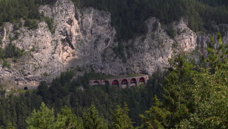 Train-running-through-tunnel-on-side-of-rocky-cliff-at-Semmering-Railway-in-Austria