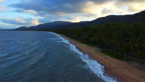 Aerial-View-Of-Coral-Sea-Waves-Splashing-On-Sandy-Beach-In-Palm-Cove,-Cairns-Region,-Queensland,-Australia-With-Overcast