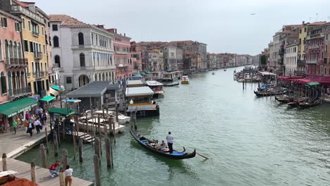 View-from-Rialto-Bridge,-Gondolier-Steering-Gondola-To-Pier-On-Grand-Canal-in-Venice,-Italy
