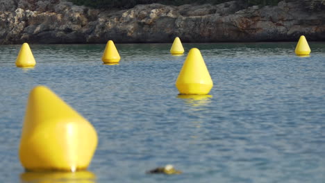 Group-of-six-yellow-conical-navigation-buoys-indicating-a-path-for-boats-in-a-rocky-cove