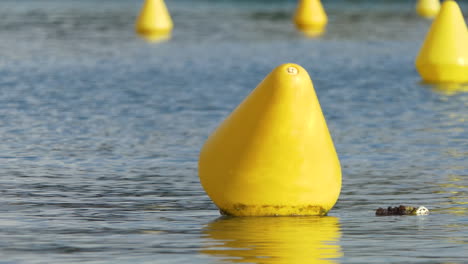 Focus-on-yellow-navigation-markers-indicating-a-way-for-ships-in-quiet-water,-background-blurred