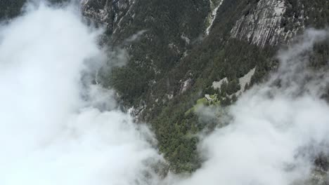 Drohnen-Luftbild,-Das-Durch-Eine-Große-Wolke-Eines-Wasserfalls-Und-Ein-Kleines-Dorf-An-Der-Seite-Eines-Berges-In-Norditalien-Fliegt