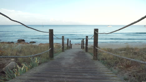 Path-with-wooden-slats-and-ropes-on-the-side-going-to-a-quiet-beach-at-dawn,-Mediterranean-Sea