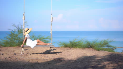 Unrecognizable-Woman-in-Sundress-and-Hat-Swinging-on-a-Big-Bench-Swing-with-Ropes-on-Amazing-Sea-View-Background-in-Thailand
