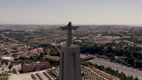 Front-facing-of-majestic-statue-of-Christ-the-King-against-Almada-cityscape,-aerial-panning-shot