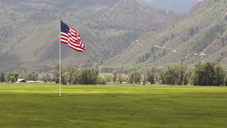 Large-American-Flag-waving-in-the-wind-over-a-grassy-field-a-ranch-house-and-mountain-trail-in-the-San-Juan-Mountains-in-background
