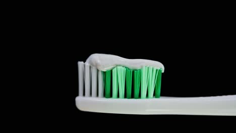 Ein-Zoom-Aus-Einer-Zahnbürste-Mit-Weißen-Und-Grünen-Borsten,-Die-Mit-Zahnpasta-Beladen-Sind-Und-Einen-Dunklen-Hintergrund-Zeigen