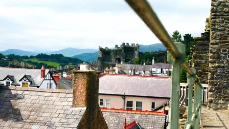Medieval-Conwy-castle-battlement-railing-walls-above-townhouse-settlement-rooftops-dolly-left