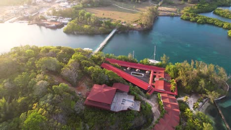 Aerial-top-view-of-tropical-island-coast,-sailboats-and-colorful-reef-,-red-roof-houses-in-Roatan-island,-Atlantida,-Honduras